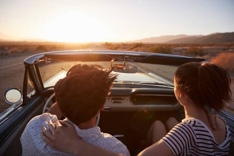 couple in a convertible driving down a road at sunset