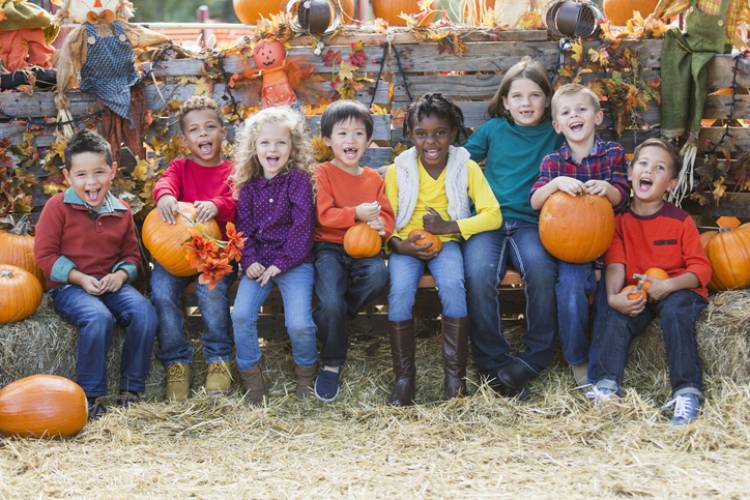 Eight kids smile and laugh on hay bales at a harvest festival