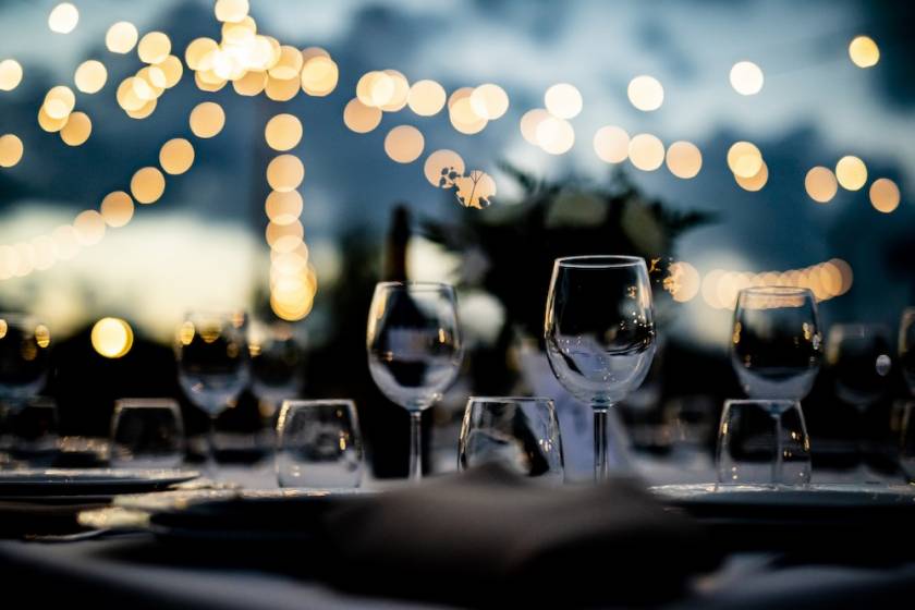 wine glasses set on a table for an outdoor dinner at a nice restaurant. blurry string lights in background